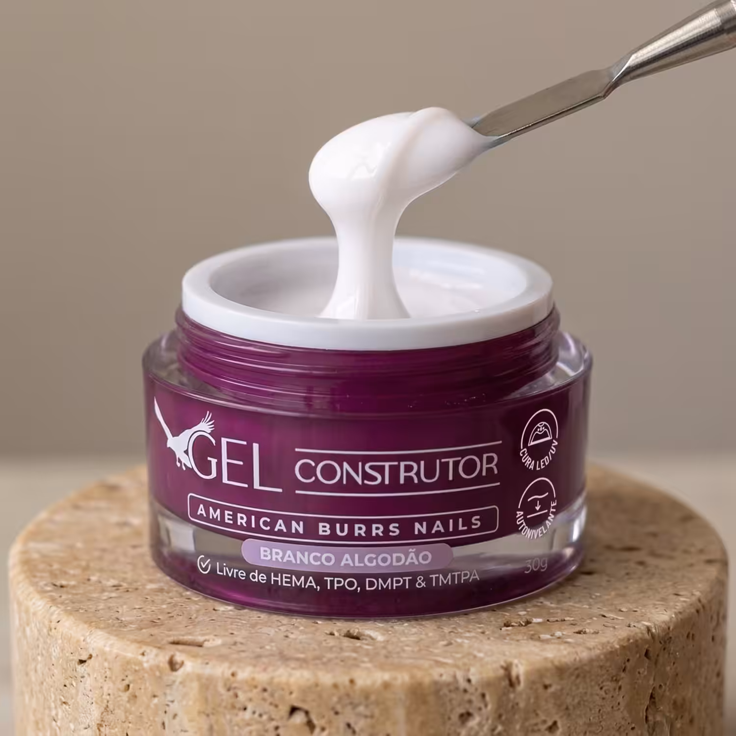 Espátula puxando o Gel Construtor Branco Algodão do pote aberto, sobre pedestal de travertino