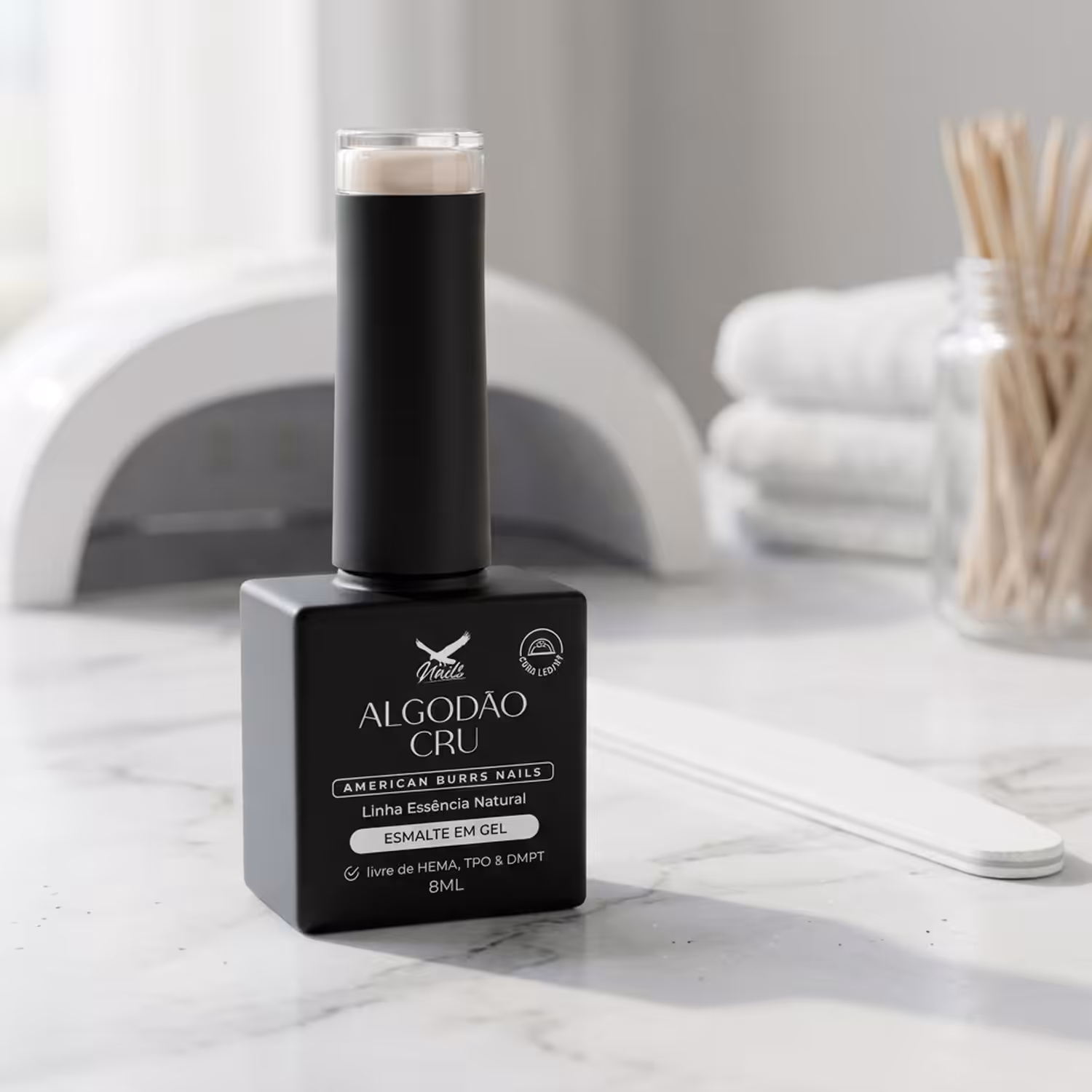 Frasco do Esmalte em Gel Algodão Cru, da Linha Essência Natural, sobre uma bancada de mármore, com uma cabine LED/UV ao fundo
