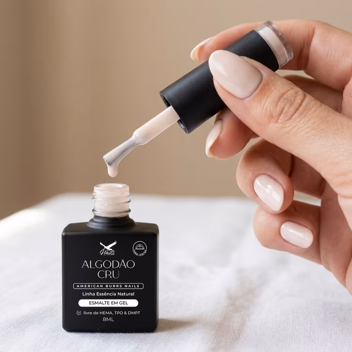 Mão segurando o pincel do Esmalte em Gel Algodão Cru sobre o frasco aberto