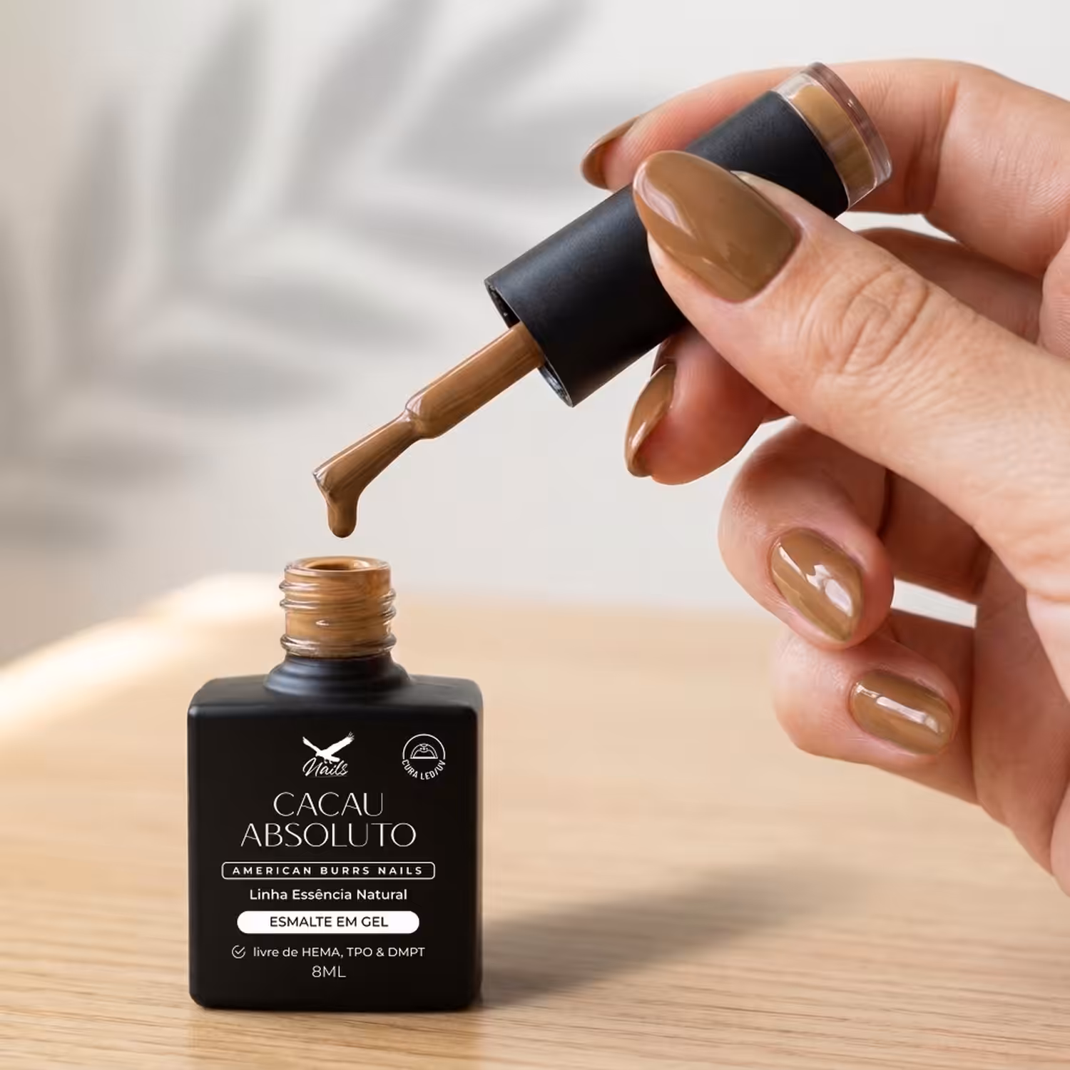 Mão segurando o pincel do Esmalte em Gel Cacau Absoluto sobre o frasco aberto