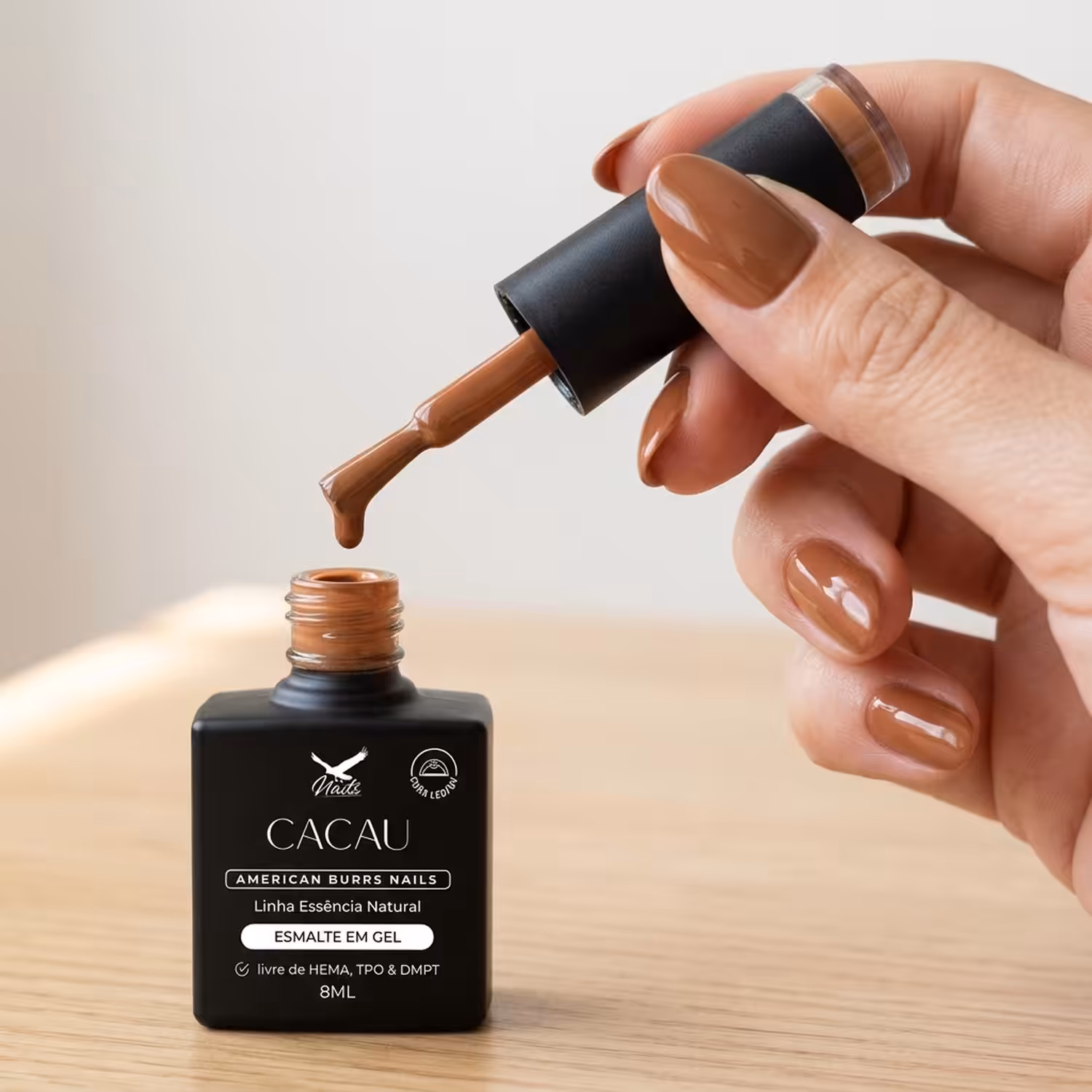 Mão segurando o pincel do Esmalte em Gel Cacau sobre o frasco aberto