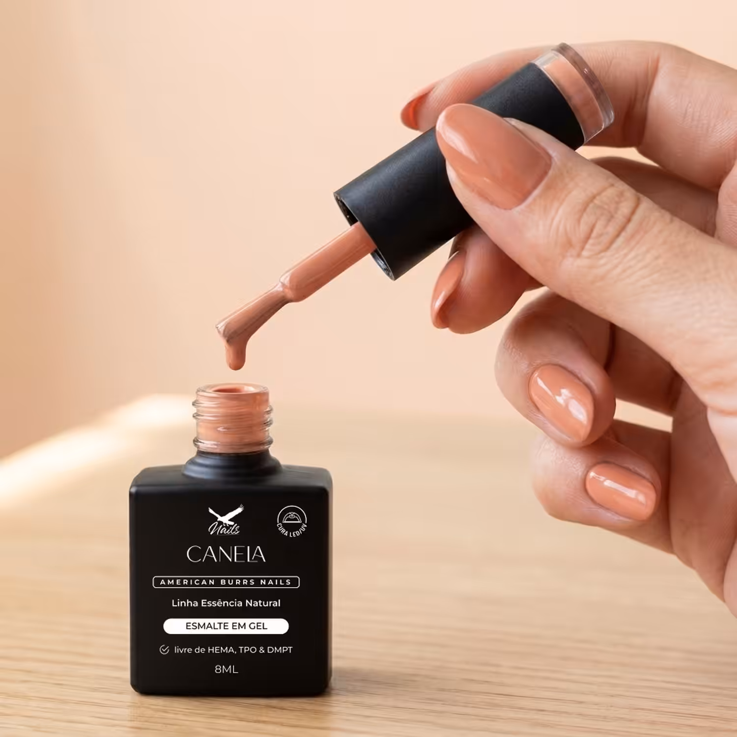Mão segurando o pincel do Esmalte em Gel Canela sobre o frasco aberto
