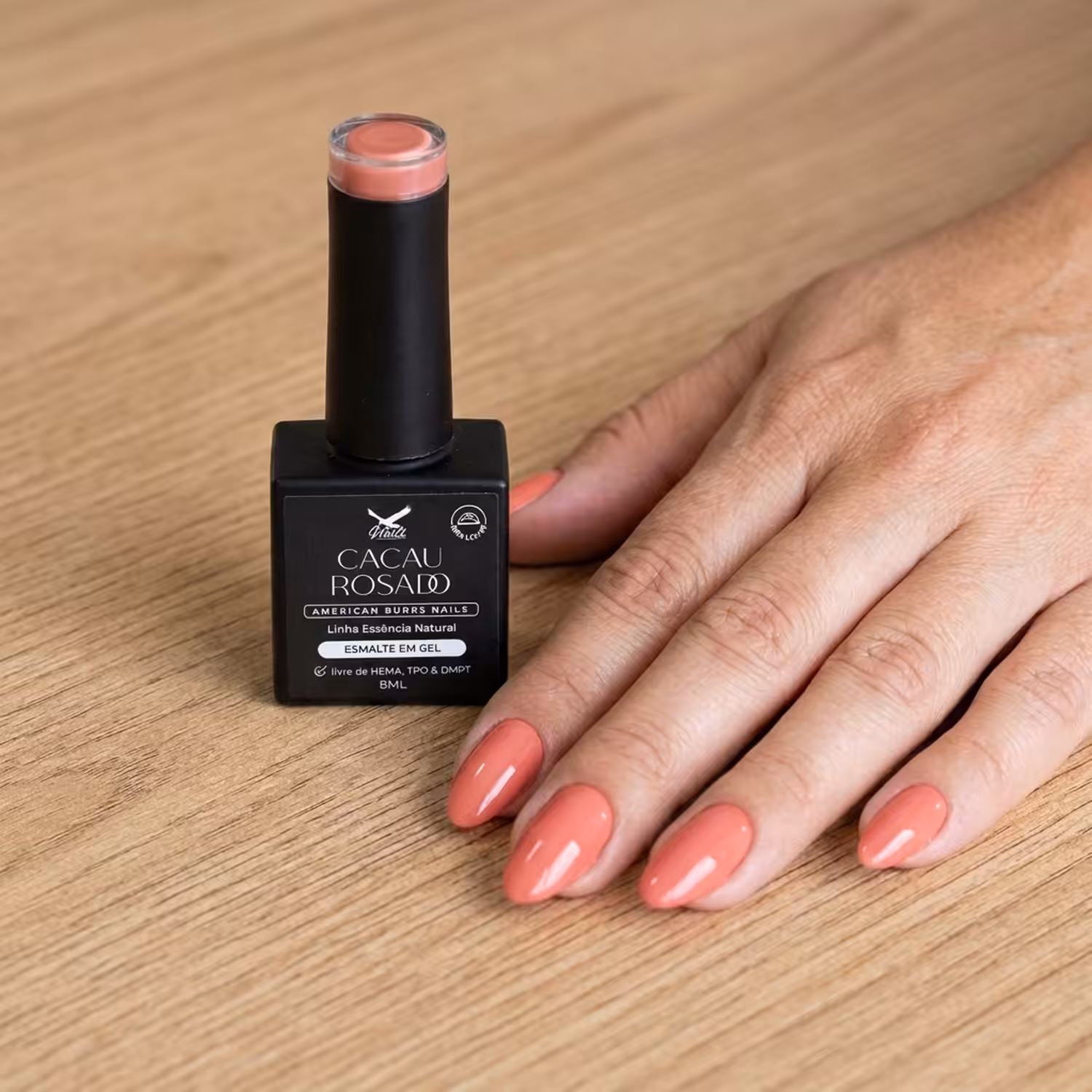 Frasco do Esmalte em Gel Cacau Rosado ao lado de uma mão apoiada na mesa, com as unhas pintadas na cor
