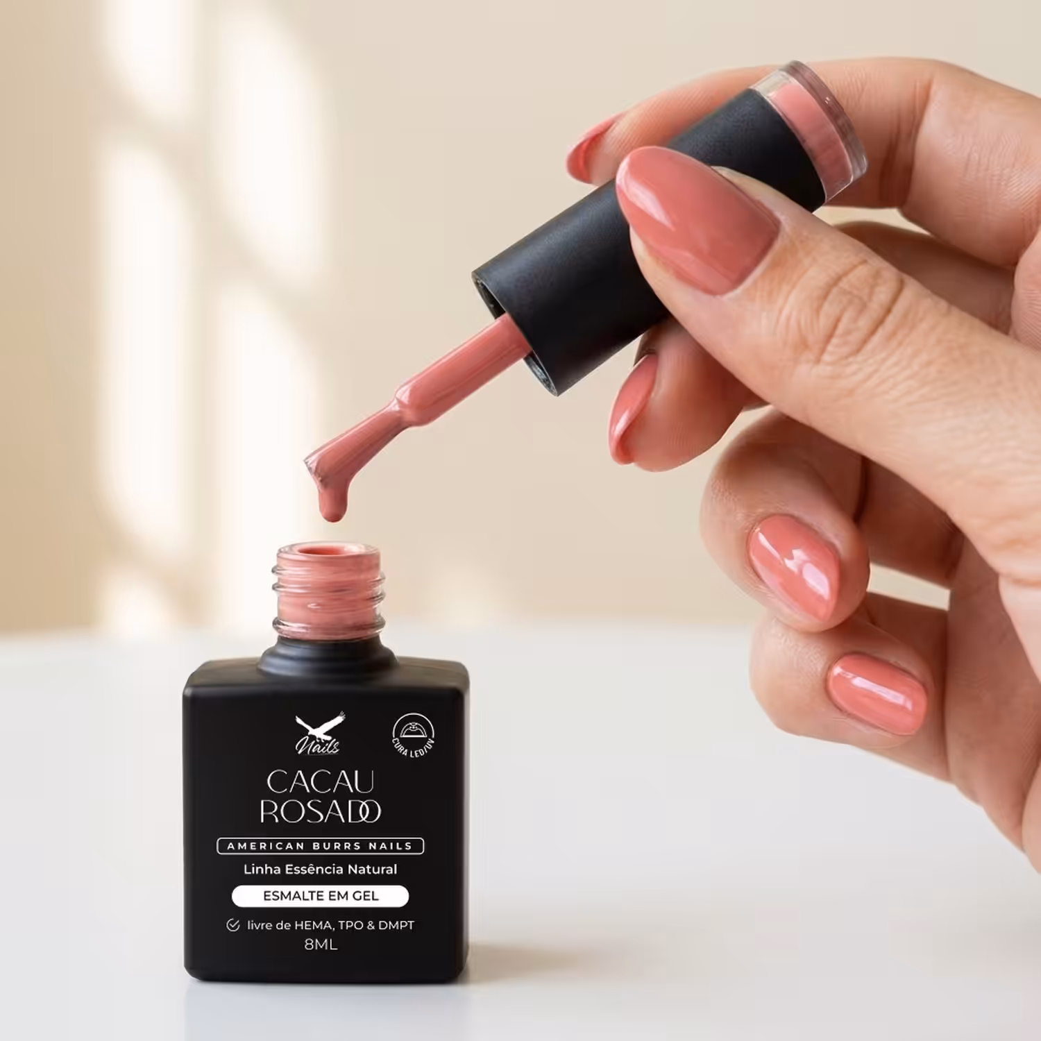 Mão segurando o pincel do Esmalte em Gel Cacau Rosado sobre o frasco aberto