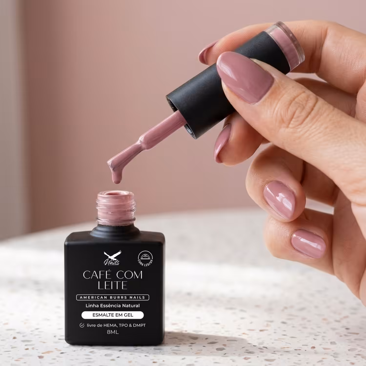 Mão segurando o pincel do Esmalte em Gel Café com Leite sobre o frasco aberto