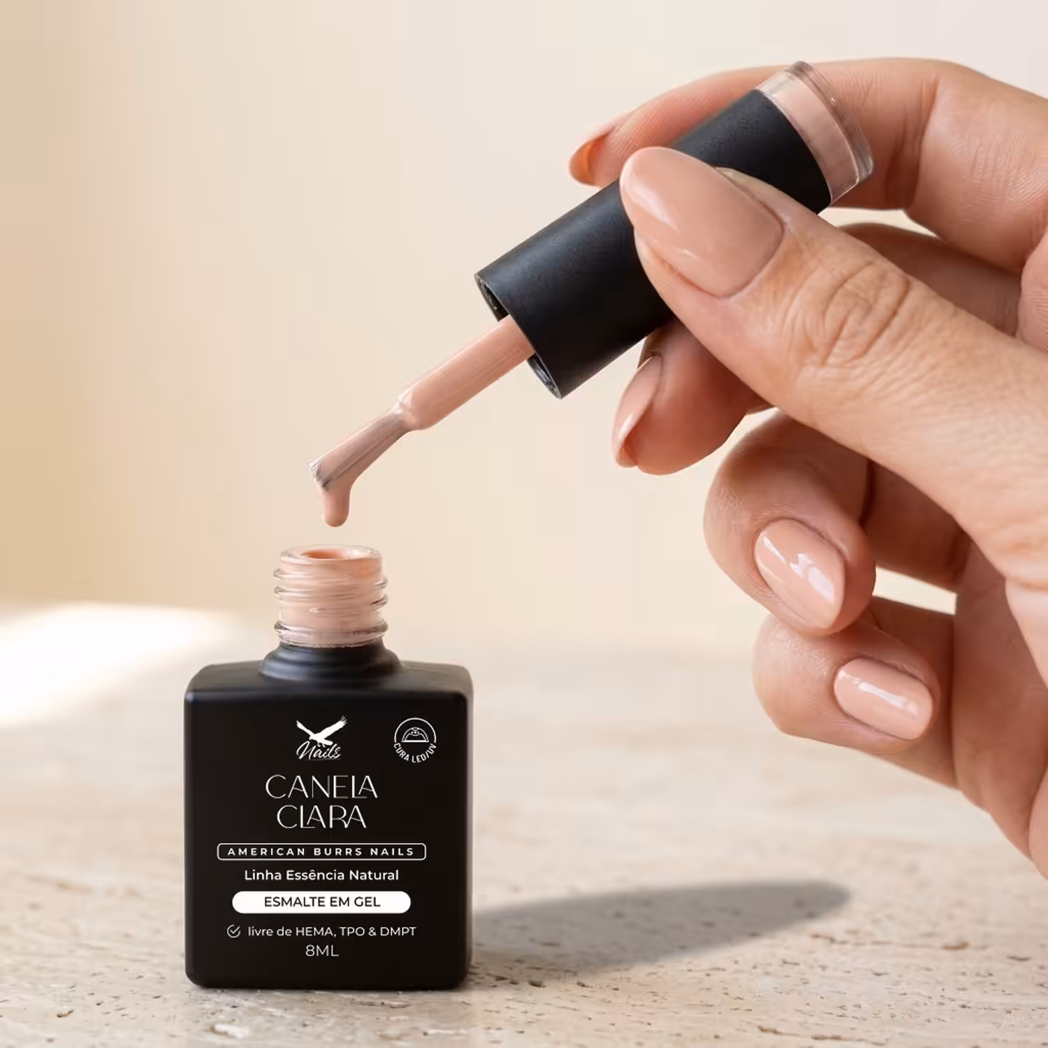 Mão segurando o pincel do Esmalte em Gel Canela Clara sobre o frasco aberto
