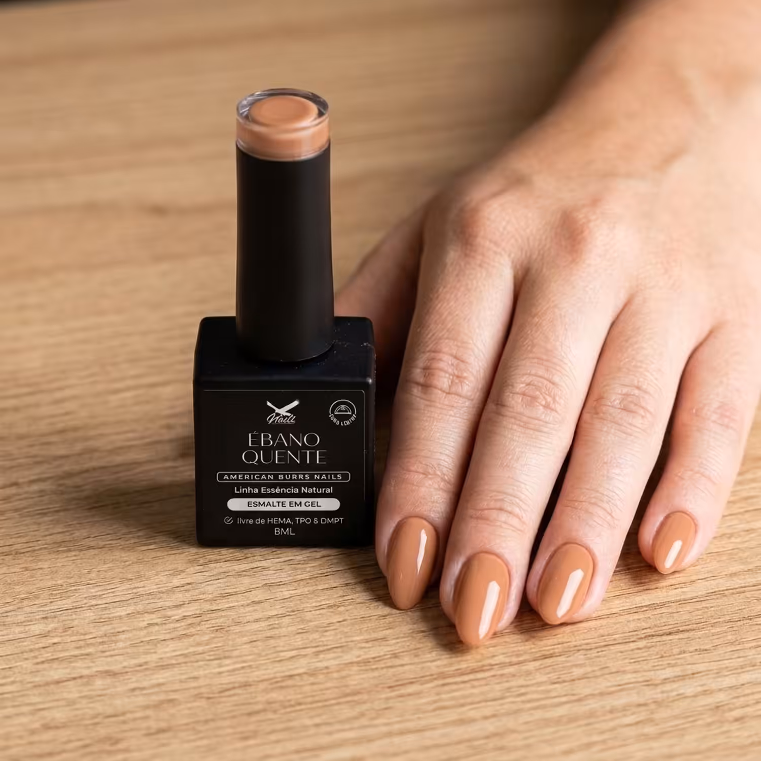 Frasco do Esmalte em Gel Ébano Quente ao lado de uma mão apoiada na mesa, com as unhas pintadas na cor