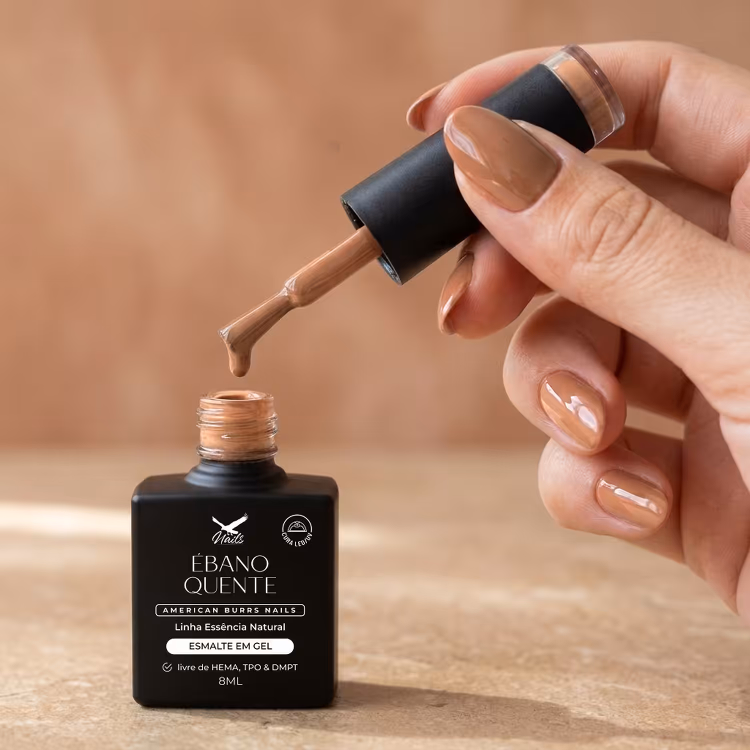 Mão segurando o pincel do Esmalte em Gel Ébano Quente sobre o frasco aberto