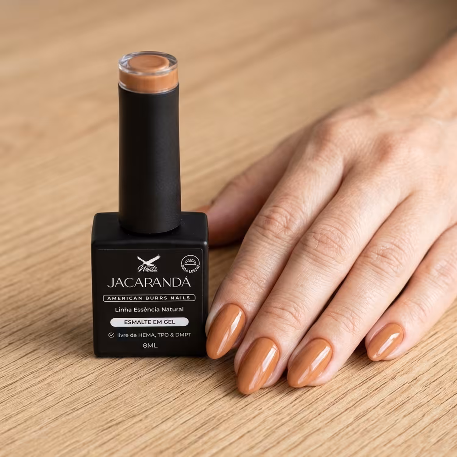 Frasco do Esmalte em Gel Jacarandá ao lado de uma mão apoiada na mesa, com as unhas pintadas na cor