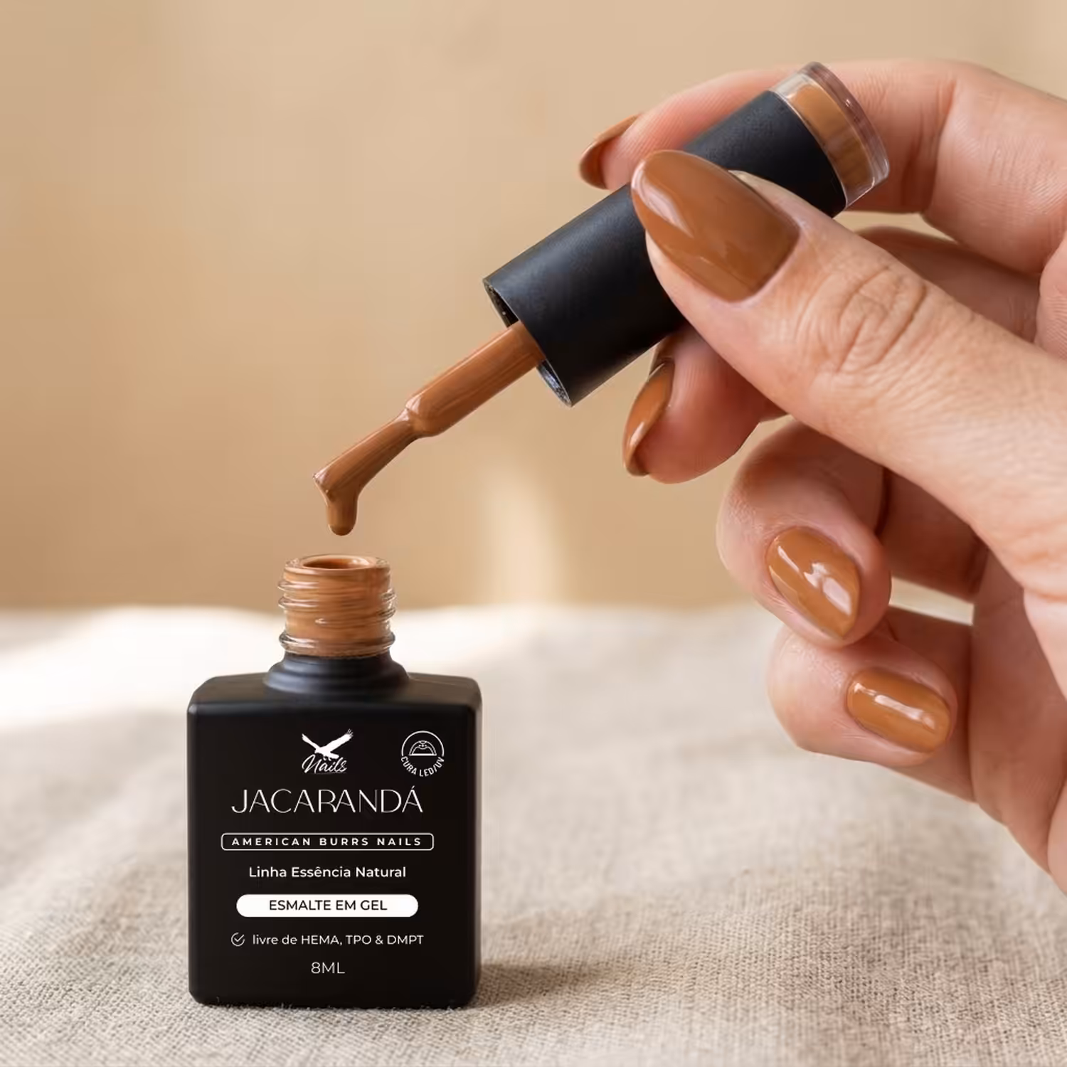 Mão segurando o pincel do Esmalte em Gel Jacarandá sobre o frasco aberto