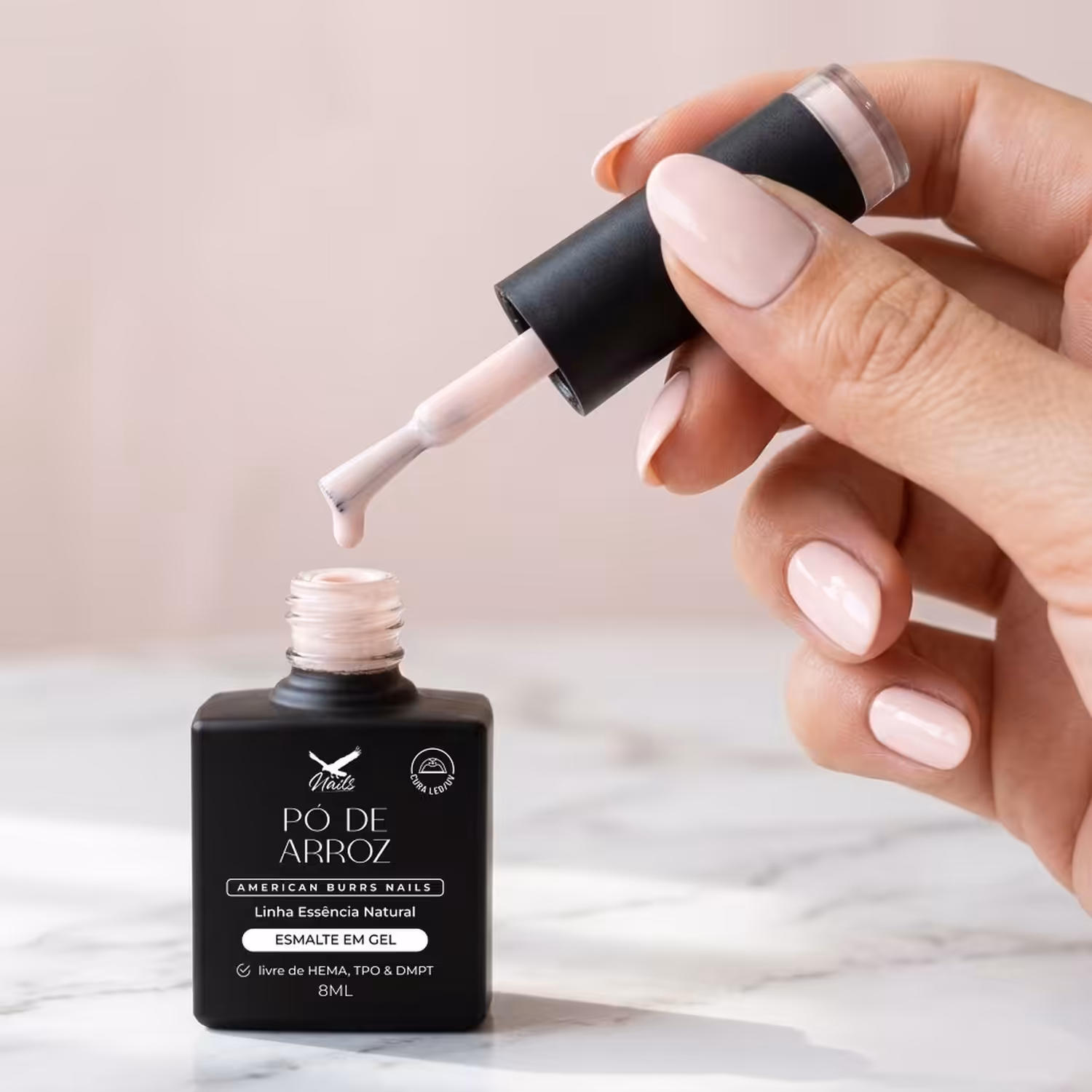 Mão segurando o pincel do Esmalte em Gel Pó de Arroz sobre o frasco aberto