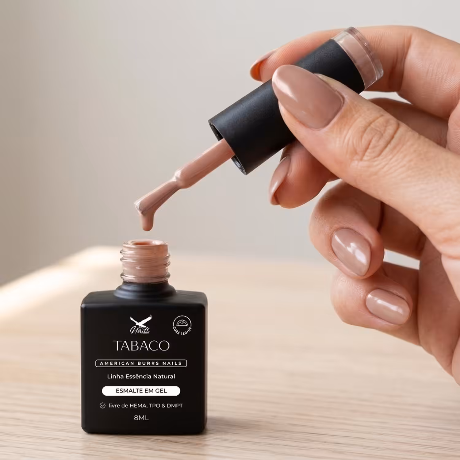 Mão segurando o pincel do Esmalte em Gel Tabaco sobre o frasco aberto
